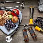	A heart-shaped plate with fruits vegetables, and grains next to exercise equipement