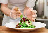 Close up photo of gloved hands preparing a salad.