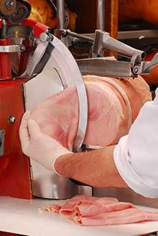 Photo of some meat being sliced with a deli meat slicer.