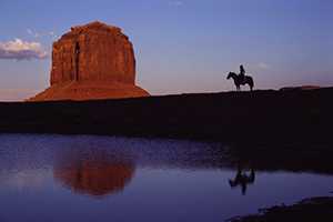 Man on horseback observes towering natural rock monument.