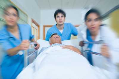	Imagen de tres médicos con batas azules empujando una camilla en la que llevan a un paciente