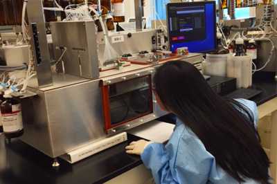 Image of a woman leaning in to see a screen as she works in a cdc laboratory.