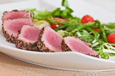 Slices of seared tuna on a plate with vegetables in the background