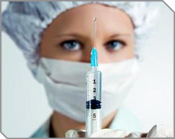medical provider wearing hair covering and face mask. Her latex gloved hand holds a syringe