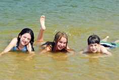image of three children laying in a shallow area of a body of water and smiling at the camera