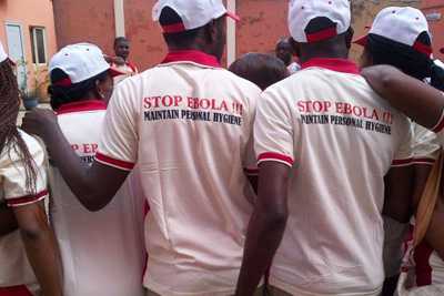 A group of “frontline” healthcare technicians in Lagos, Nigeria, wearing white t-shirts displaying the phrase, “STOP EBOLA!!! MAINTAIN PERSONAL HYGIENE” in red.