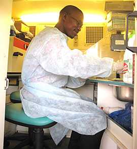 Photo: Oubote Abodji (Agence de Médicine Préventive) working inside the LaboMobil®, performing on-site cultures, gram stains, and biochemical identification tests at Lazaret during April 2015