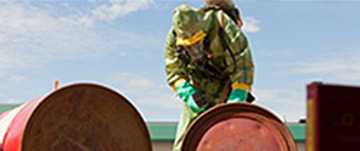 	An individual in a biohazard suit working with barrels