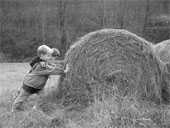 two children pushing against a round bale of hay