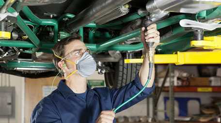 Auto worker wearing filtering facepiece respirator, protective eye wear, and hearing protection.