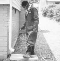 worker spraying termiticide at base of a building under a downspout