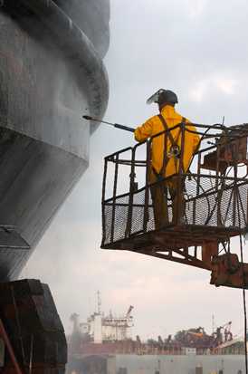 A worker pressure washes a vessel prior to repair