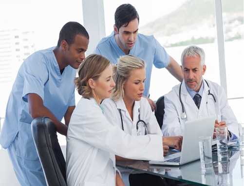 A group of healthcare workers huddle around a laptop computer