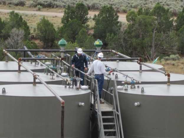 workers inspect oil production tanks