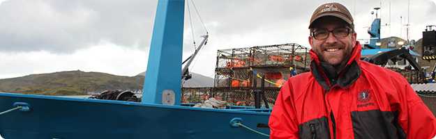 	An image of a NIOSH researcher posing for photo in front of a Bering Sea crab vessel in Dutch Harbor, AK