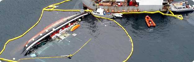 	Aerial photo of a partially submerged commercial vessel with oil containment booms surrounding the vessel and a larger vessel beginning salvage operations.