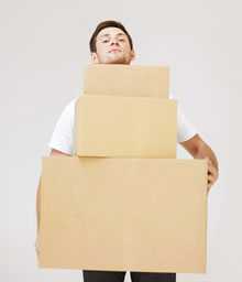 	A young man struggles to carry three oversized boxes.