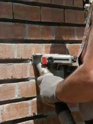 	Bricklayer using a tuck-pointing grinder equipped with an on-tool dust control to remove mortar from a brick wall