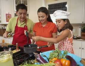 A girl cooking a meal with her parents.