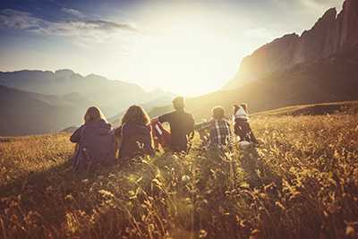 Group of people in a field watching the sun set behind mountains