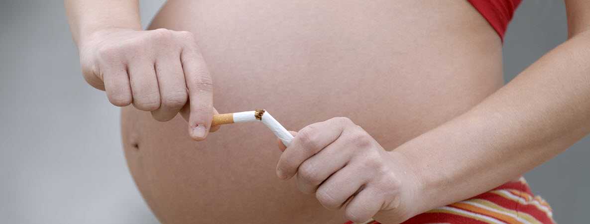image of a pregnant woman's belly and her hands breaking a cigarette in half. 