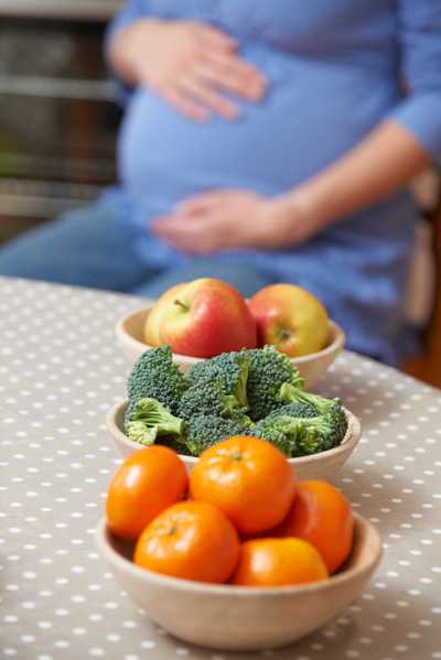 Pregnant Woman Looking At Bowls Of Healthy Fruit And Vegetables 