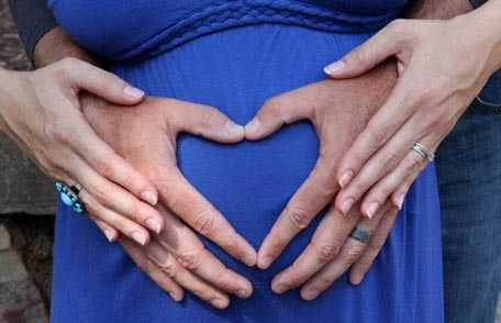 Imagen de las manos de una mujer embarazada y las de su marido formando un corazón en el vientre