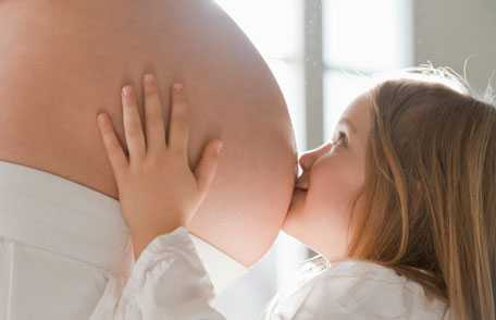 Una niña besando el vientre de una mujer embarazada