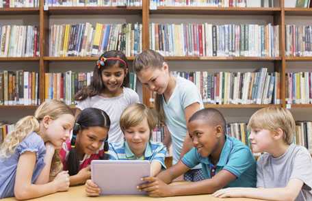 niños en una biblioteca reunidos alrededor de un ordenador portátil