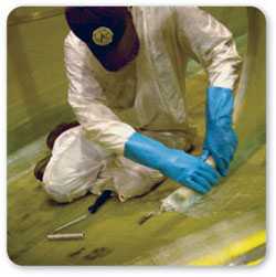 Vista delantera de un trabajador arrodillado usando guantes de caucho al aplicar barniz en el suelo