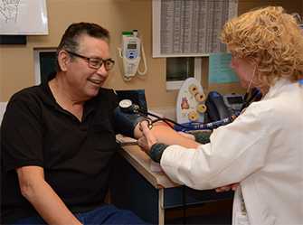 Un paciente con un manguito en el brazo está sentado al lado de una enfermera que le toma la presión arterial.