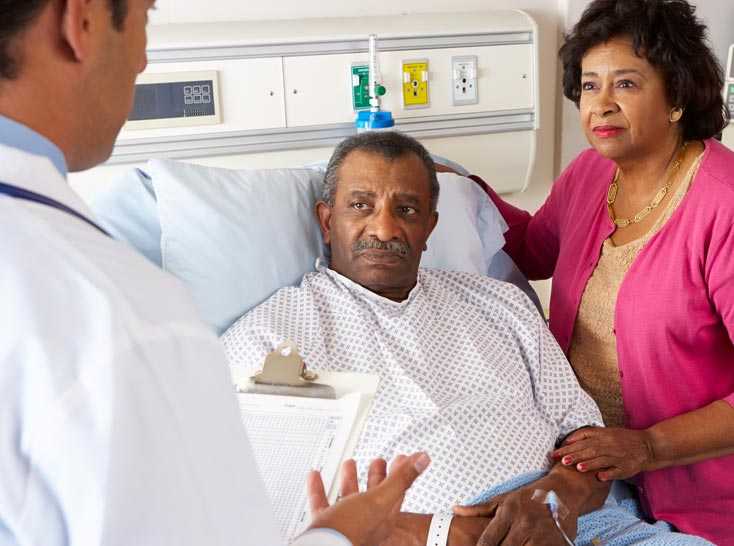 Un médico habla con un paciente que está sentado en una cama de hospital. 