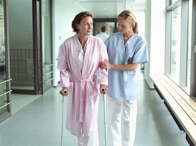 A woman using crutches to walk with the aid of a nurse.
