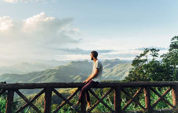 Man sitting on a wooden fence with mountains in the background