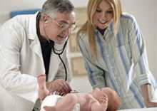Un médico escucha el latido del corazón de un bebé por medio de un estetoscopio mientras la madre los mira.