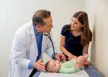 Un médico escucha el latido del corazón de un bebé por medio de un estetoscopio mientras la madre los mira.