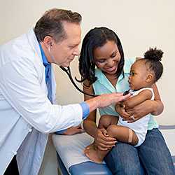 Male doctor with a stethoscope listens to a child’s heartbeat, as the mother holds the child.