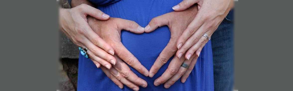 Pregnant woman with her husbands hand in the shape of a heart on her belly.